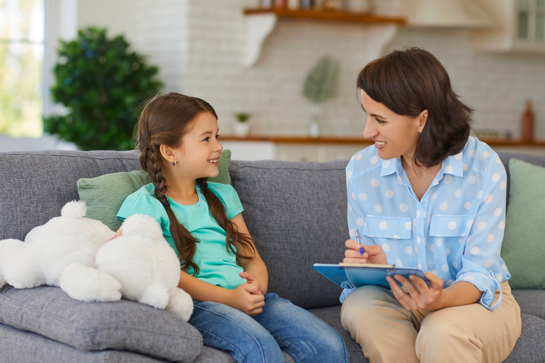 Happy Little Child Communicating with Psychologist Sitting on Sofa during Therapy Session at Home